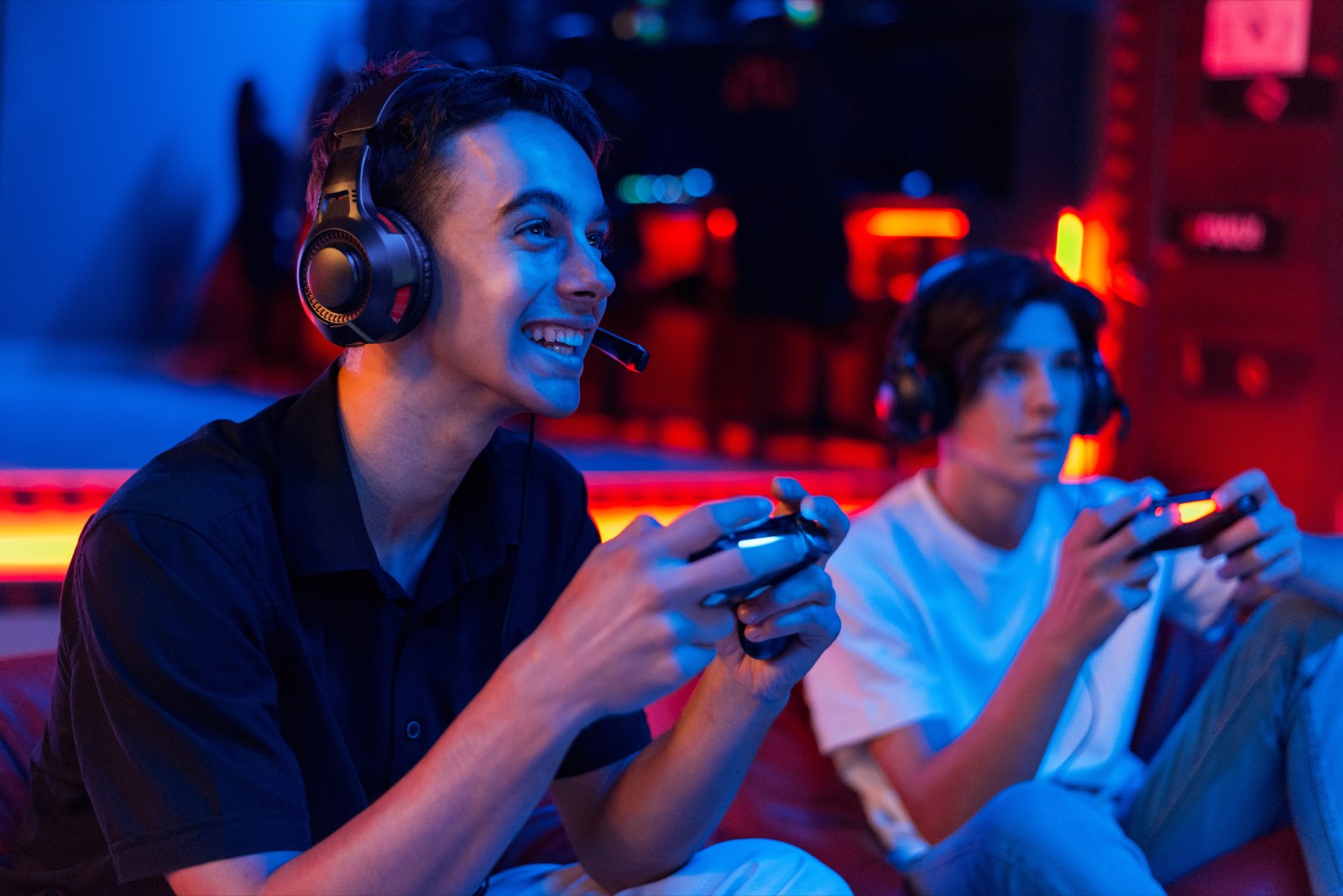 Two players on beanbags in a neon-lit gaming lounge, controllers in hand.
